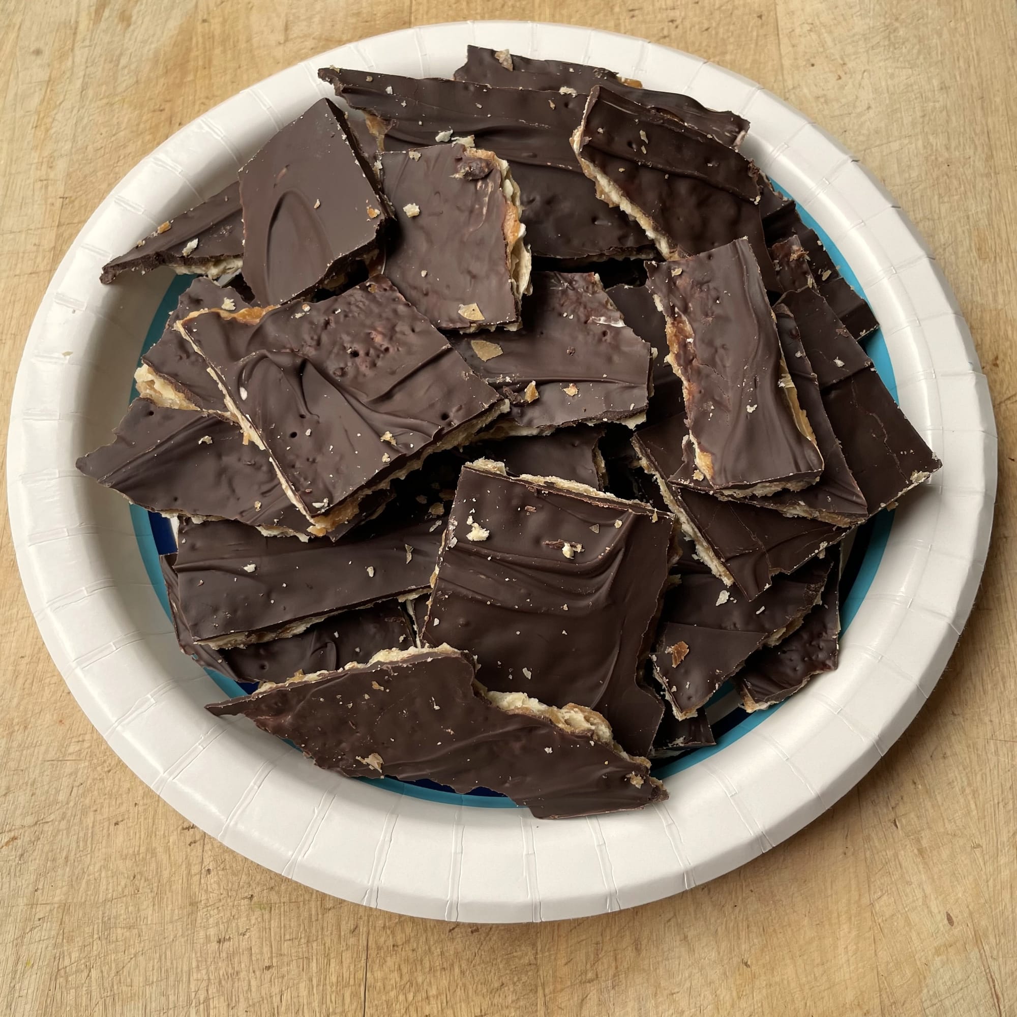 Paper plate piled with pieces of matzah toffee, a crisp cracker with a layer of toffee and a chocolate topping